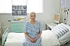Eldre kvinne sitter på en oppredd sykehusseng i et lyst pasientrom.